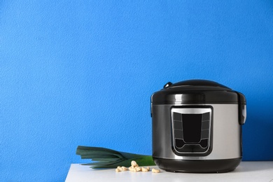 Modern multi cooker and ingredients on table near color wall, space for text