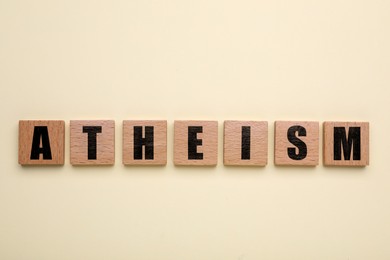 Image of Word Atheism made of wooden squares with letters on beige background, top view