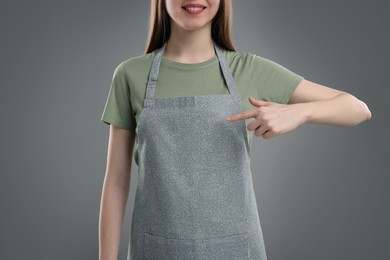 Woman pointing at kitchen apron on grey background, closeup. Mockup for design