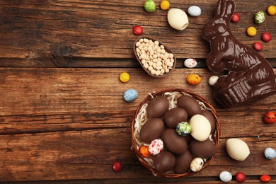 Photo of Chocolate Easter bunny and eggs on wooden table, flat lay. Space for text