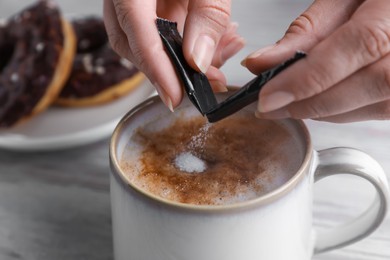 Woman adding sugar to tasty coffee at white wooden table, closeup