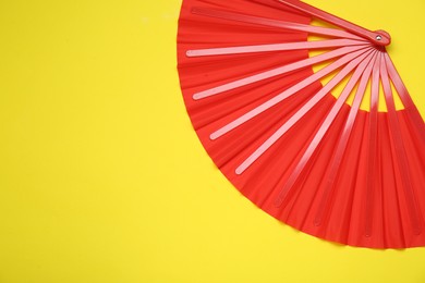 Photo of Bright red hand fan on yellow background, top view. Space for text