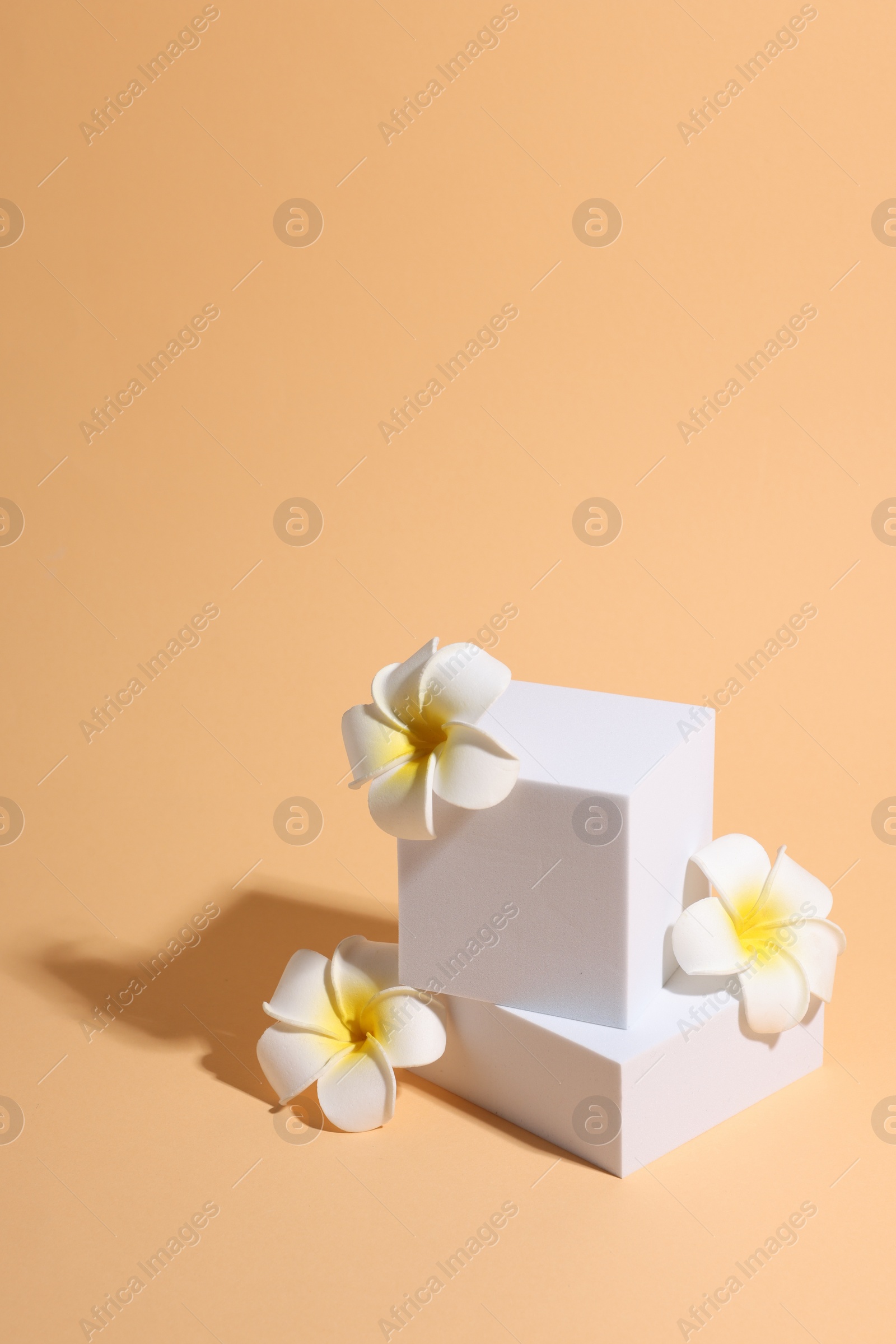 Photo of Scene with podium for product presentation. Figures of different geometric shapes and flowers on pale orange background