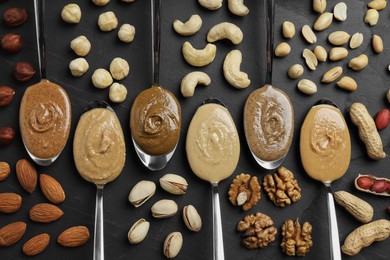 Tasty nut butters in spoons and raw nuts on dark gray table, flat lay