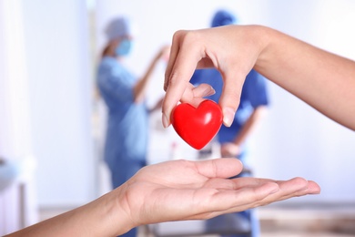 Doctor giving red heart to patient, closeup. Donation day