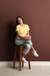 Photo of Beautiful young woman sitting on stool near brown wall