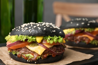 Photo of Tasty burgers with black buns on board, closeup