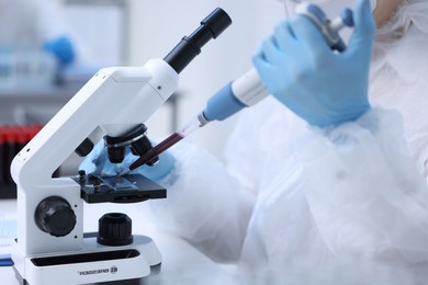 Scientist dripping sample onto glass slide while working with microscope in laboratory, closeup