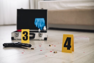 Photo of Crime scene markers, gun and criminologist case on floor in room