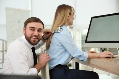 Photo of Young man sticking paper fish to colleague's back in office. Funny joke