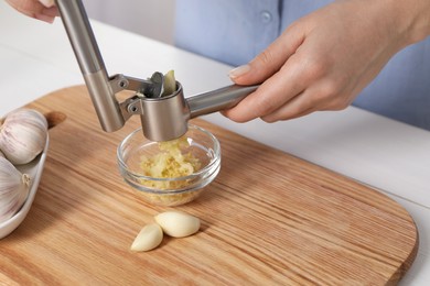 Photo of Woman squeezing garlic with press at white table, closeup
