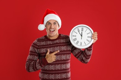 Photo of Man in Santa hat with clock on red background. New Year countdown