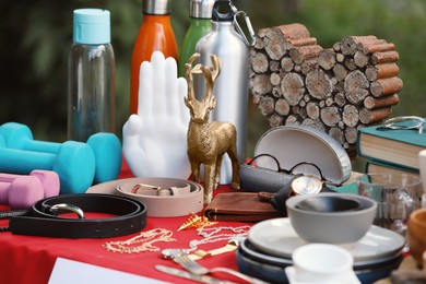 Photo of Many different items on red tablecloth outdoors. Garage sale