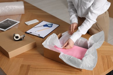 Photo of Seller packing clothes into cardboard box at table in office, closeup. Online store