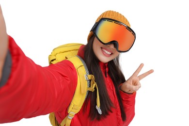 Photo of Smiling woman in ski goggles taking selfie and showing peace sign on white background