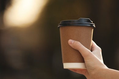 Woman with takeaway coffee cup outdoors, closeup. Space for text