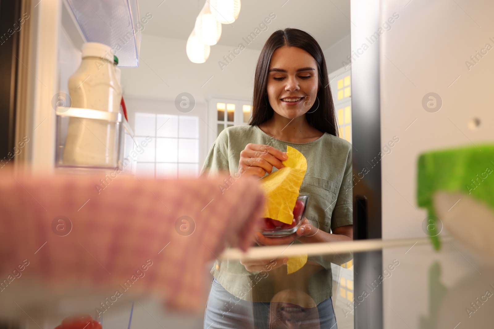 Photo of Happy woman taking away beeswax food wrap, view from refrigerator
