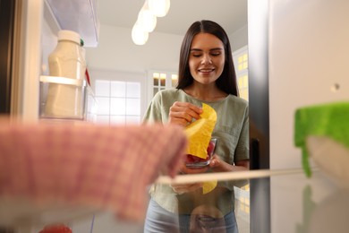 Happy woman taking away beeswax food wrap, view from refrigerator