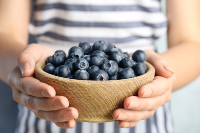 Photo of Woman holding fresh ripe blueberries in wooden bowl, closeup