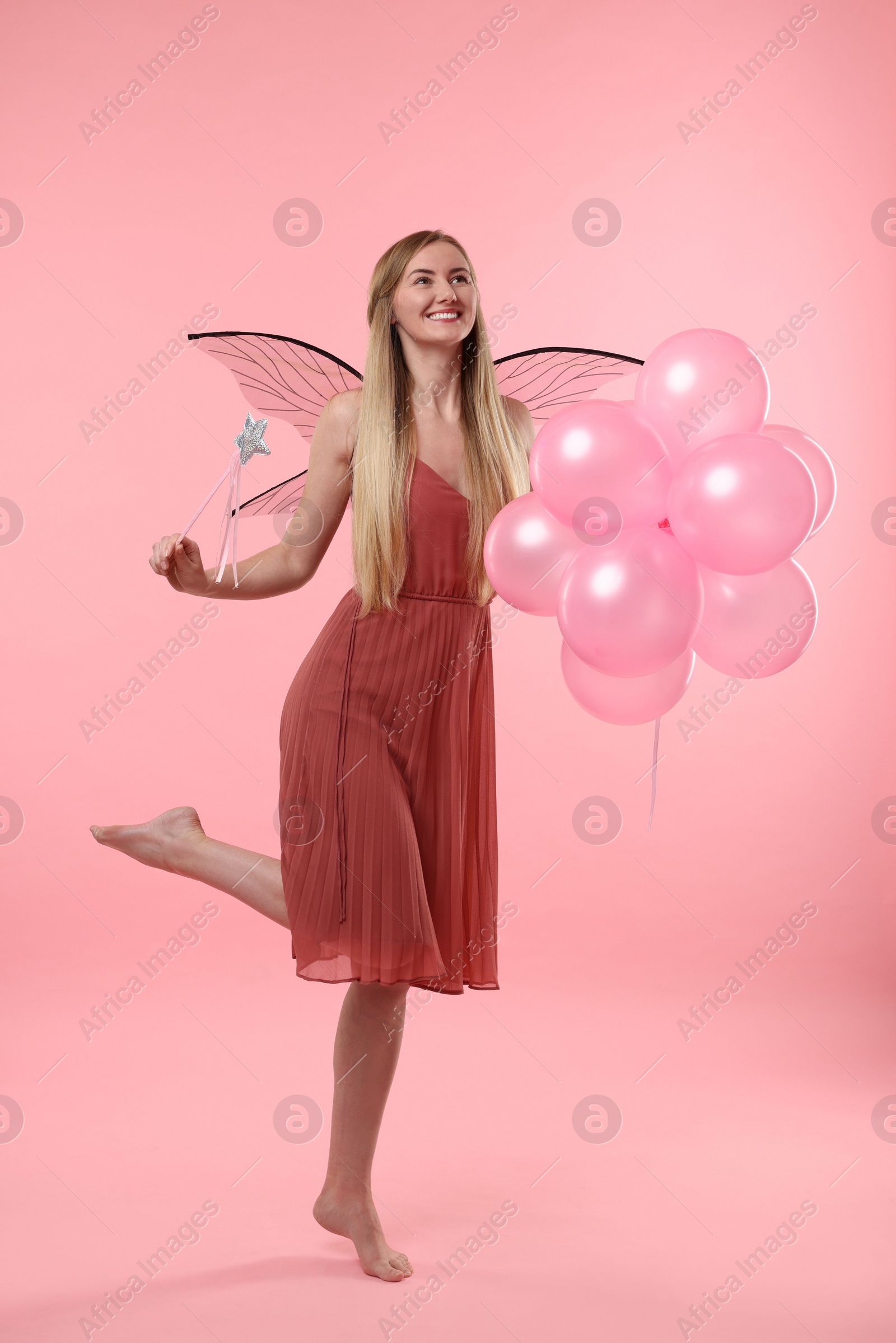 Photo of Beautiful girl in fairy costume with wings, magic wand and balloons on pink background