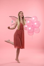 Beautiful girl in fairy costume with wings, magic wand and balloons on pink background