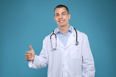 Young man in white coat with stethoscope on color background