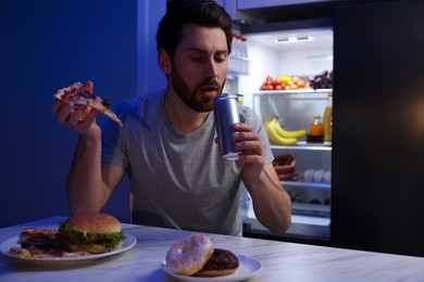 Man drinking soda and eating junk food in kitchen at night. Bad habit