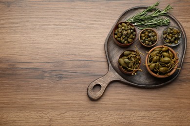 Photo of Delicious pickled capers and rosemary twigs on wooden table, top view. Space for text