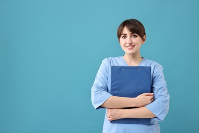 Portrait of smiling medical assistant with clipboard on light blue background. Space for text