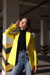 Fashionable young woman wearing stylish outfit with yellow jacket in open parking garage