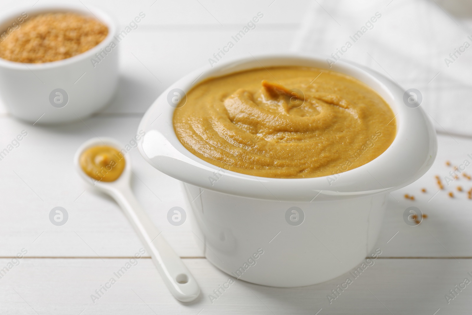 Photo of Tasty mustard sauce in bowl on white wooden table, closeup