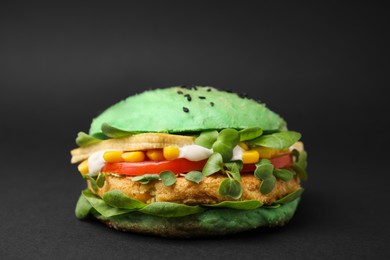 Photo of Tasty green vegan burger with vegetables, patty and microgreens on black background, closeup