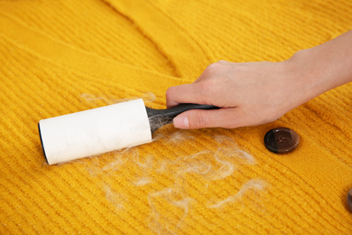 Photo of Woman removing hair from yellow knitted jacket with lint roller, closeup