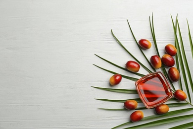 Photo of Palm oil in glass bowl, tropical leaf and fruits on white wooden table, flat lay. Space for text