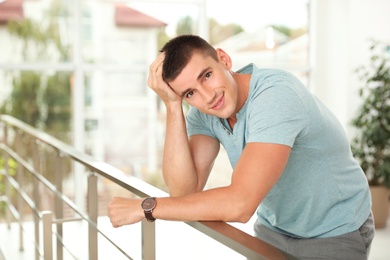 Portrait of handsome young man leaning on railing indoors