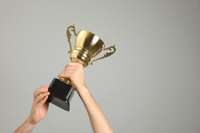 Photo of Man holding gold trophy cup on light grey background, closeup. Space for text