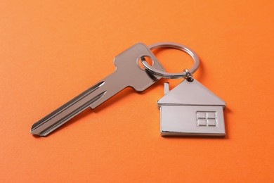 Photo of Metallic key with keychain in shape of house on orange background
