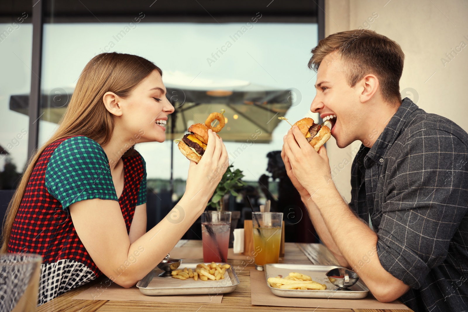 Photo of Young couple eating burgers in street cafe