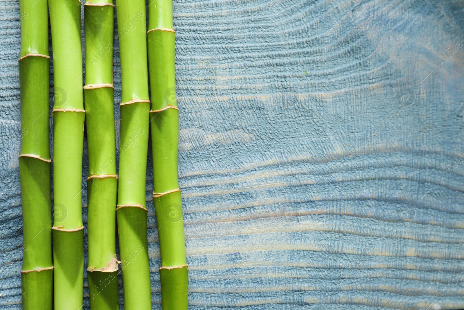 Photo of Green bamboo stems and space for text on wooden background, top view