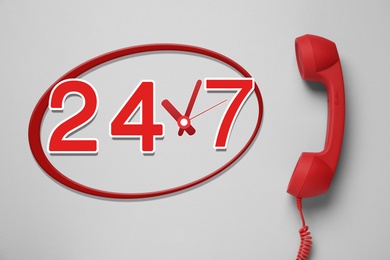 Image of 24/7 hotline service. Red handset on light grey background, top view