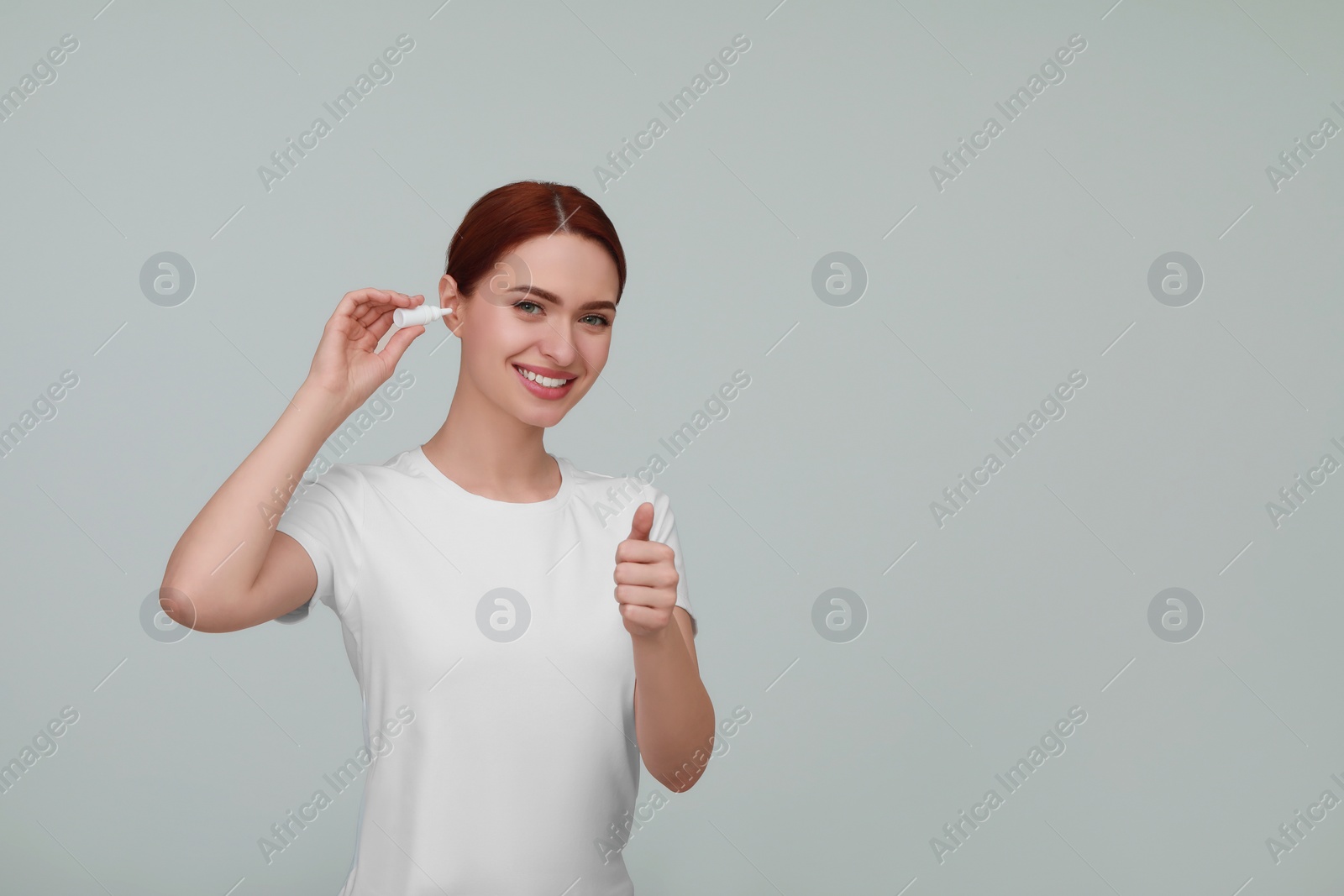 Photo of Woman using ear drops on light grey background. Space for text