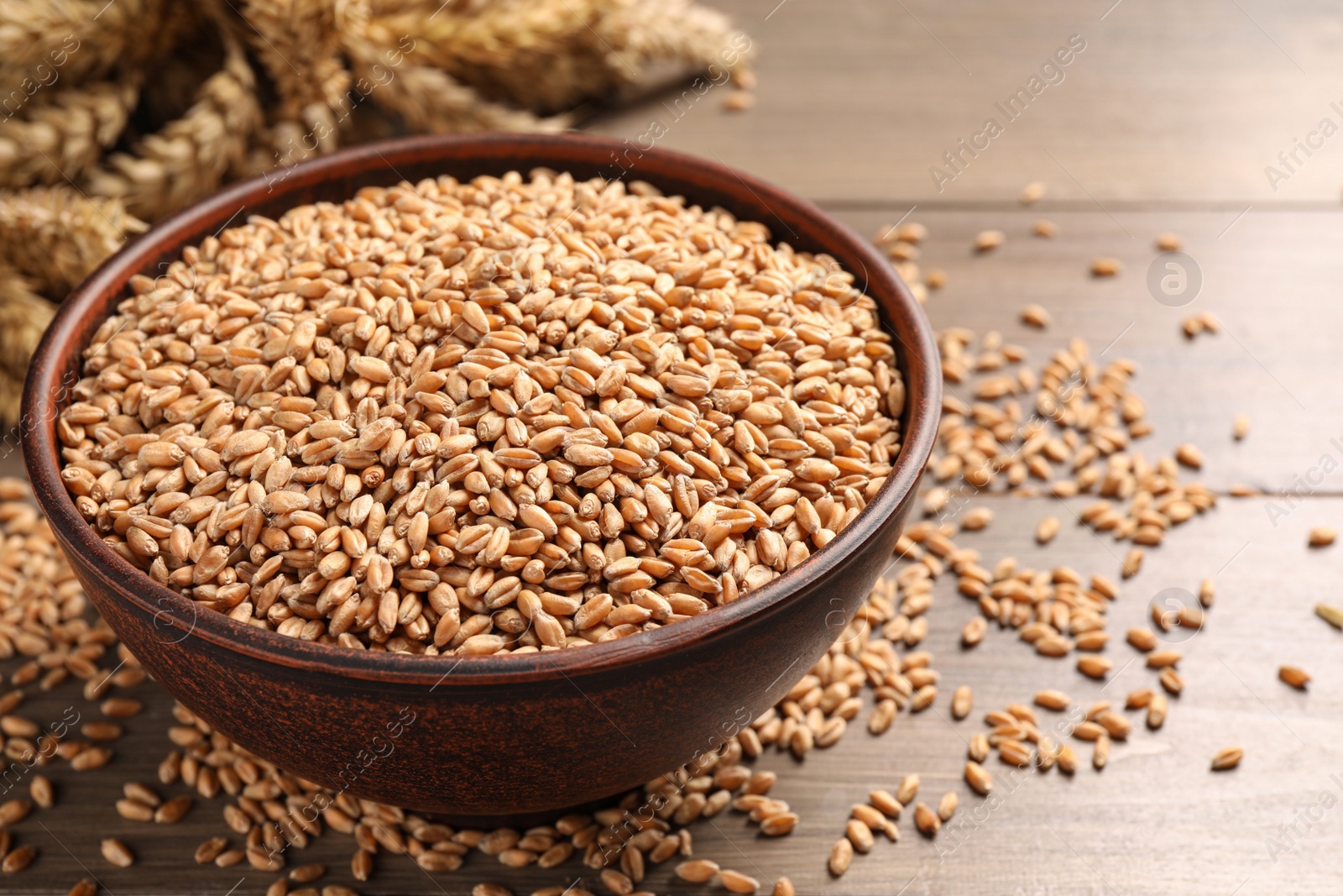 Photo of Wheat grains in bowl on wooden table, closeup