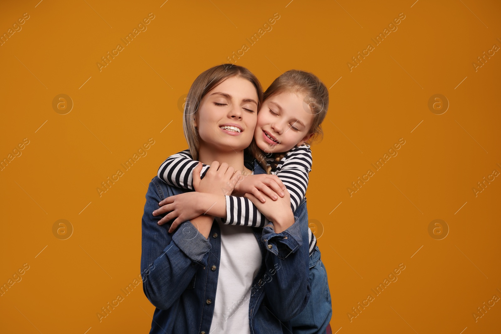 Photo of Little daughter hugging her mom on orange background. Happy Mother's Day
