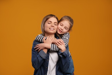 Little daughter hugging her mom on orange background. Happy Mother's Day
