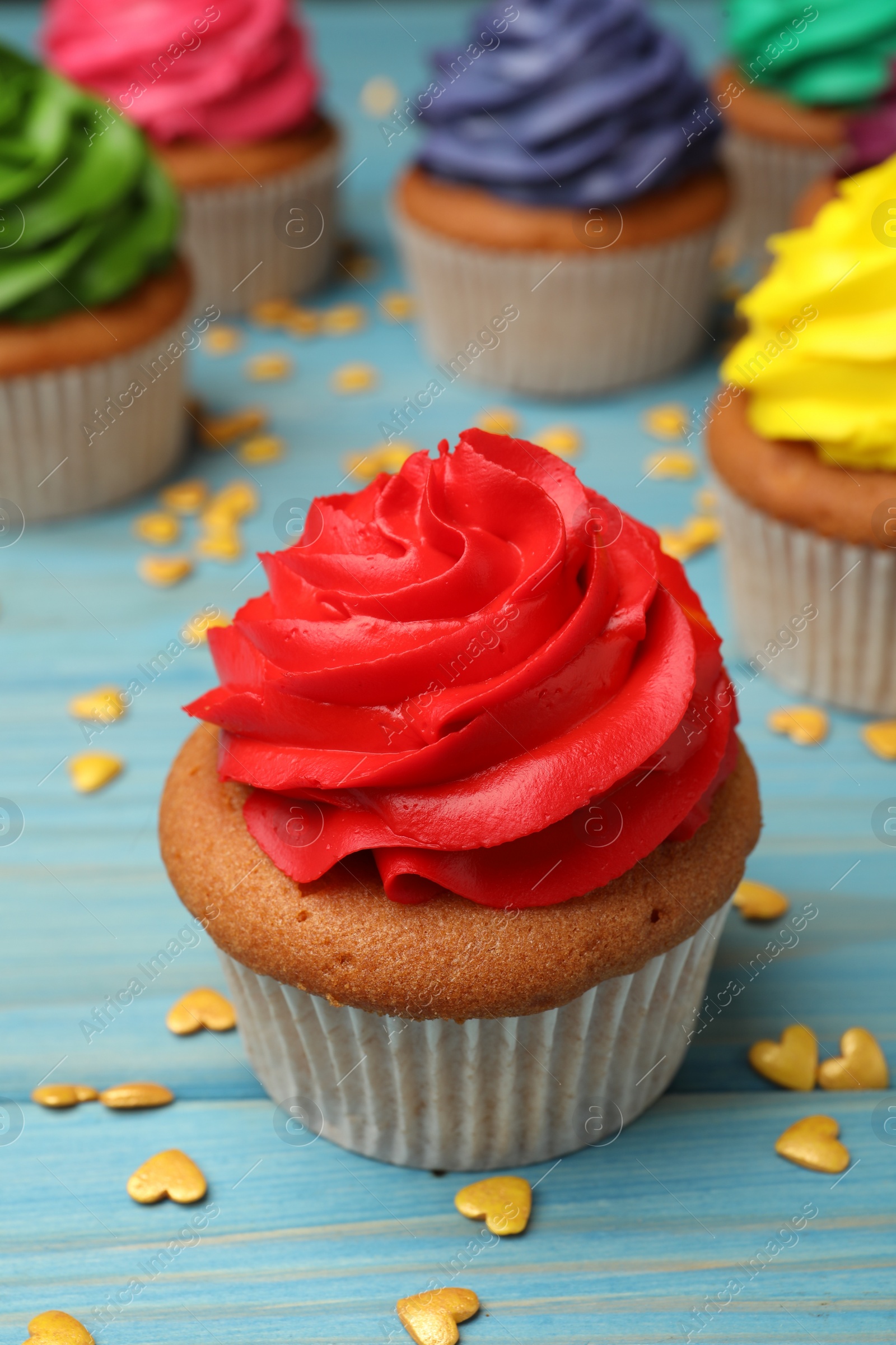 Photo of Delicious cupcake with red cream and heart shaped sprinkles on light blue wooden table