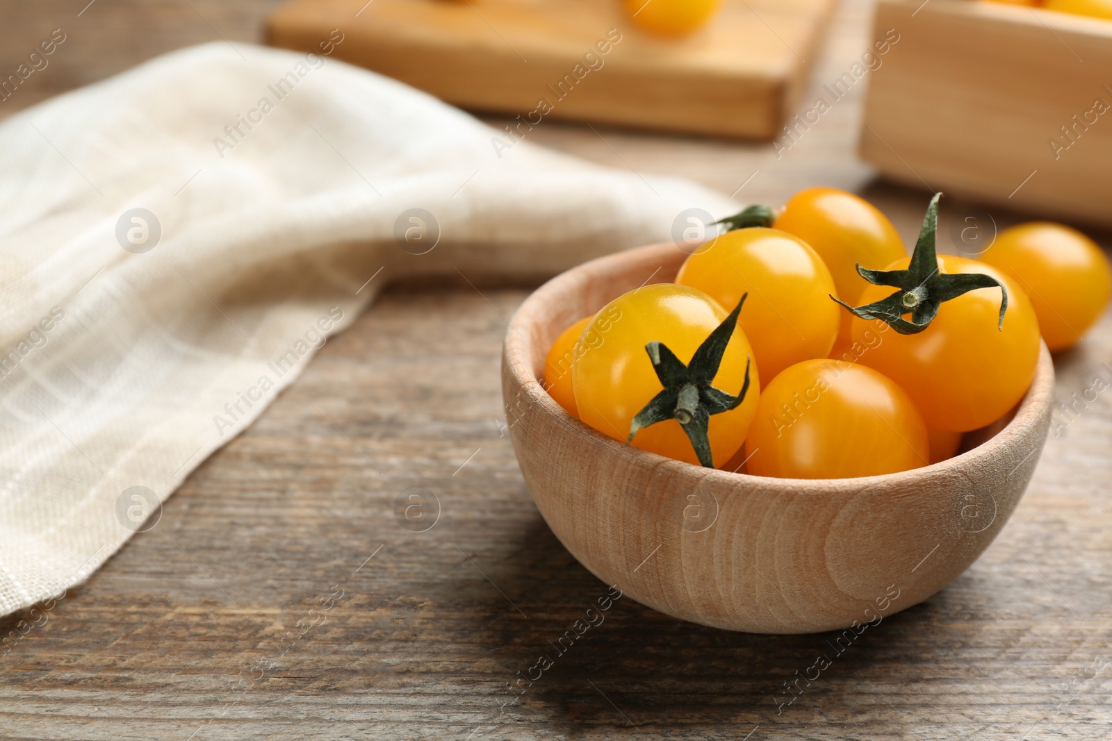 Photo of Ripe yellow tomatoes in bowl on wooden table