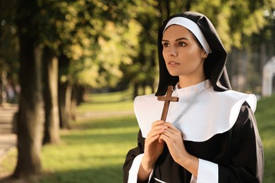 Young nun with Christian cross in park on sunny day, space for text