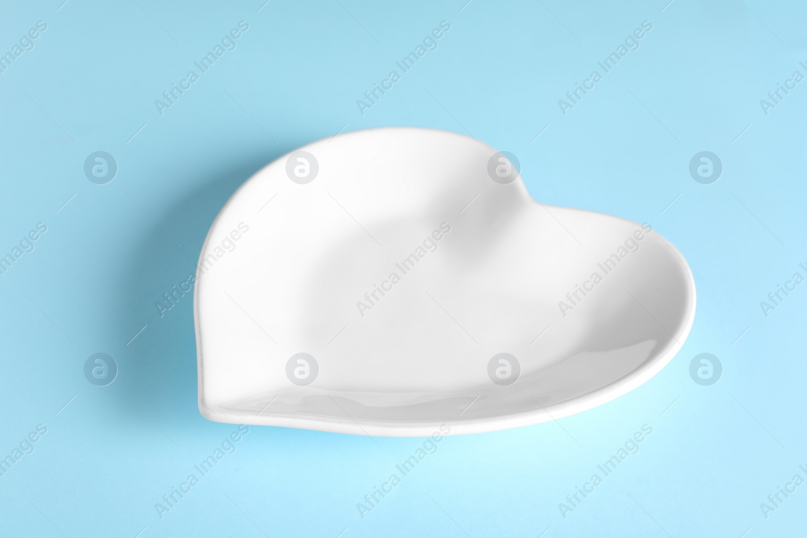 Photo of Heart shaped ceramic plate on light blue background, closeup