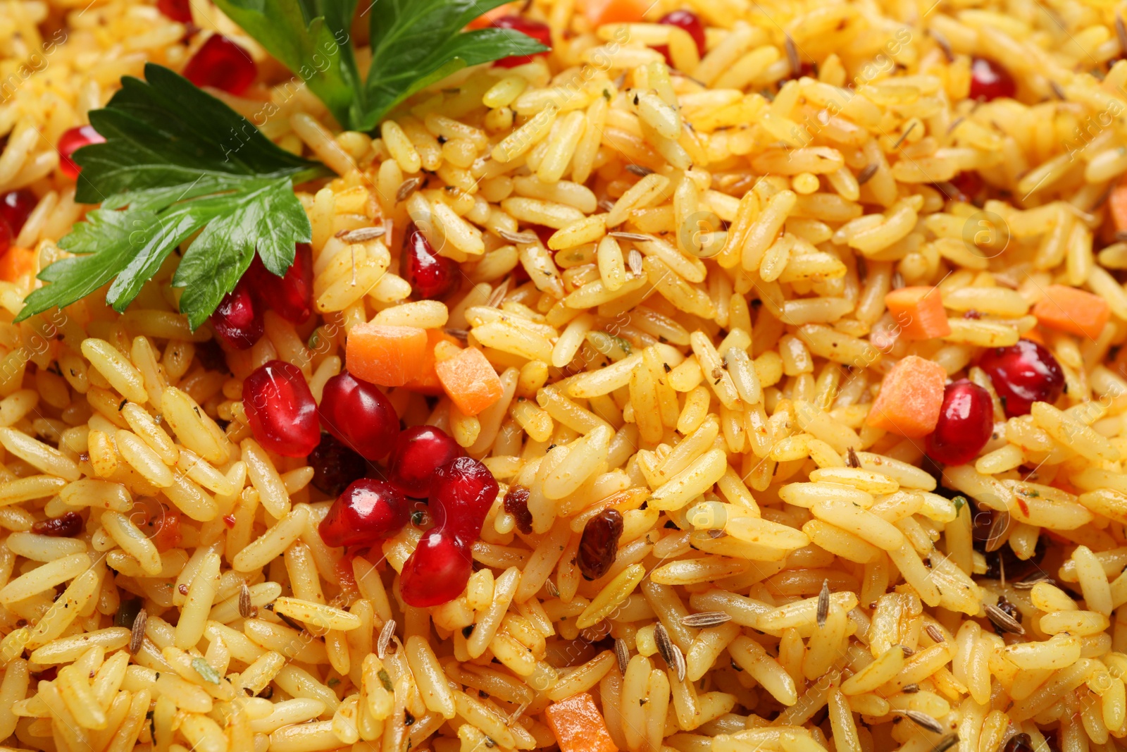 Photo of Tasty rice pilaf with pomegranate grains and parsley as background, closeup