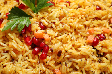 Photo of Tasty rice pilaf with pomegranate grains and parsley as background, closeup